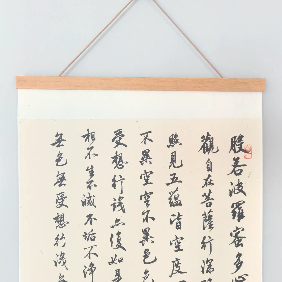 Handwritten Heart Sutra Chinese calligraphy hanging scroll with teak rods, displayed on a minimal white wall.