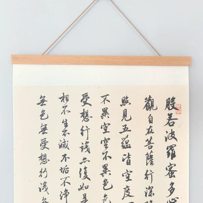 Handwritten Heart Sutra Chinese calligraphy hanging scroll with teak rods, displayed on a minimal white wall.