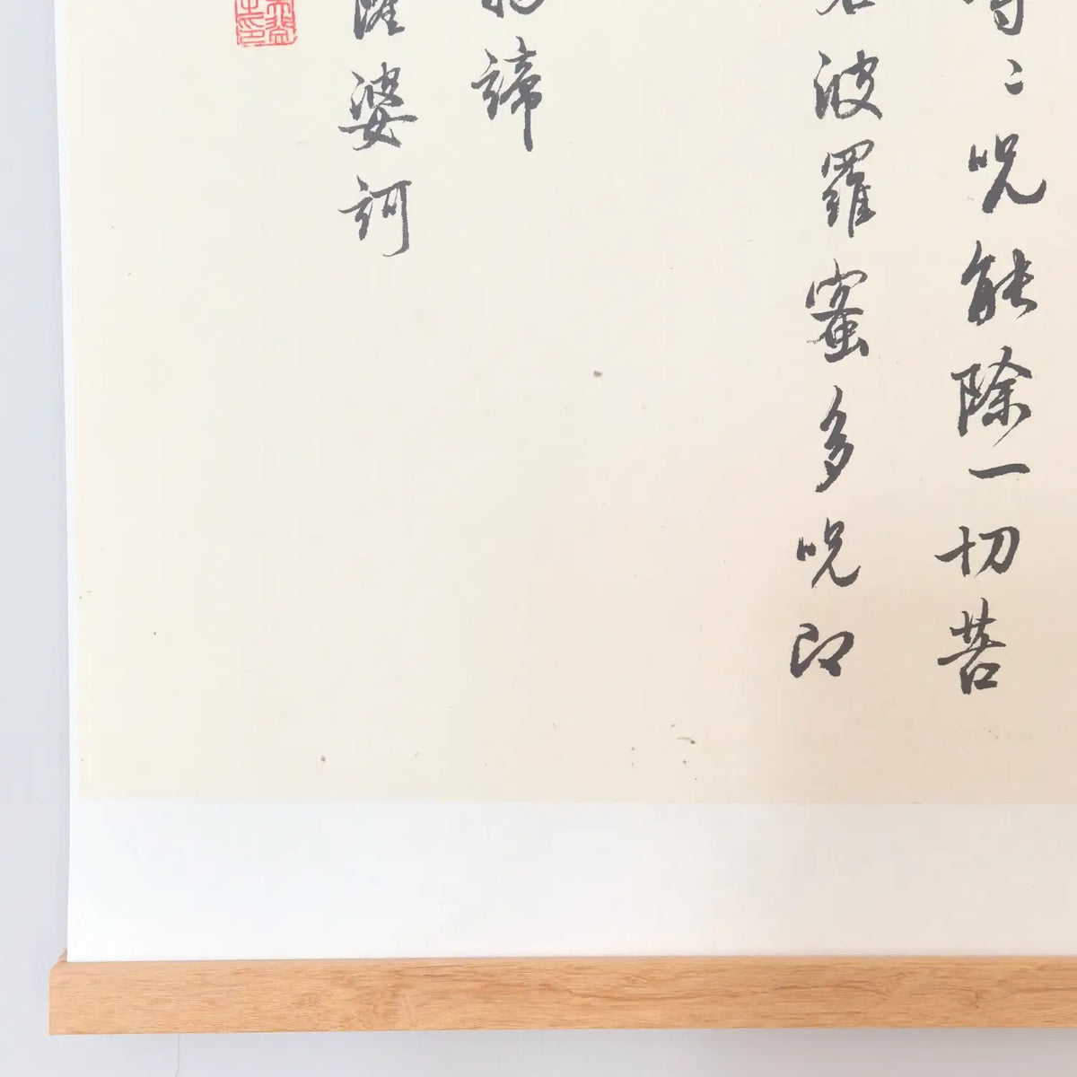 Handwritten Heart Sutra Chinese calligraphy hanging scroll with teak rods, displayed on a minimal white wall.