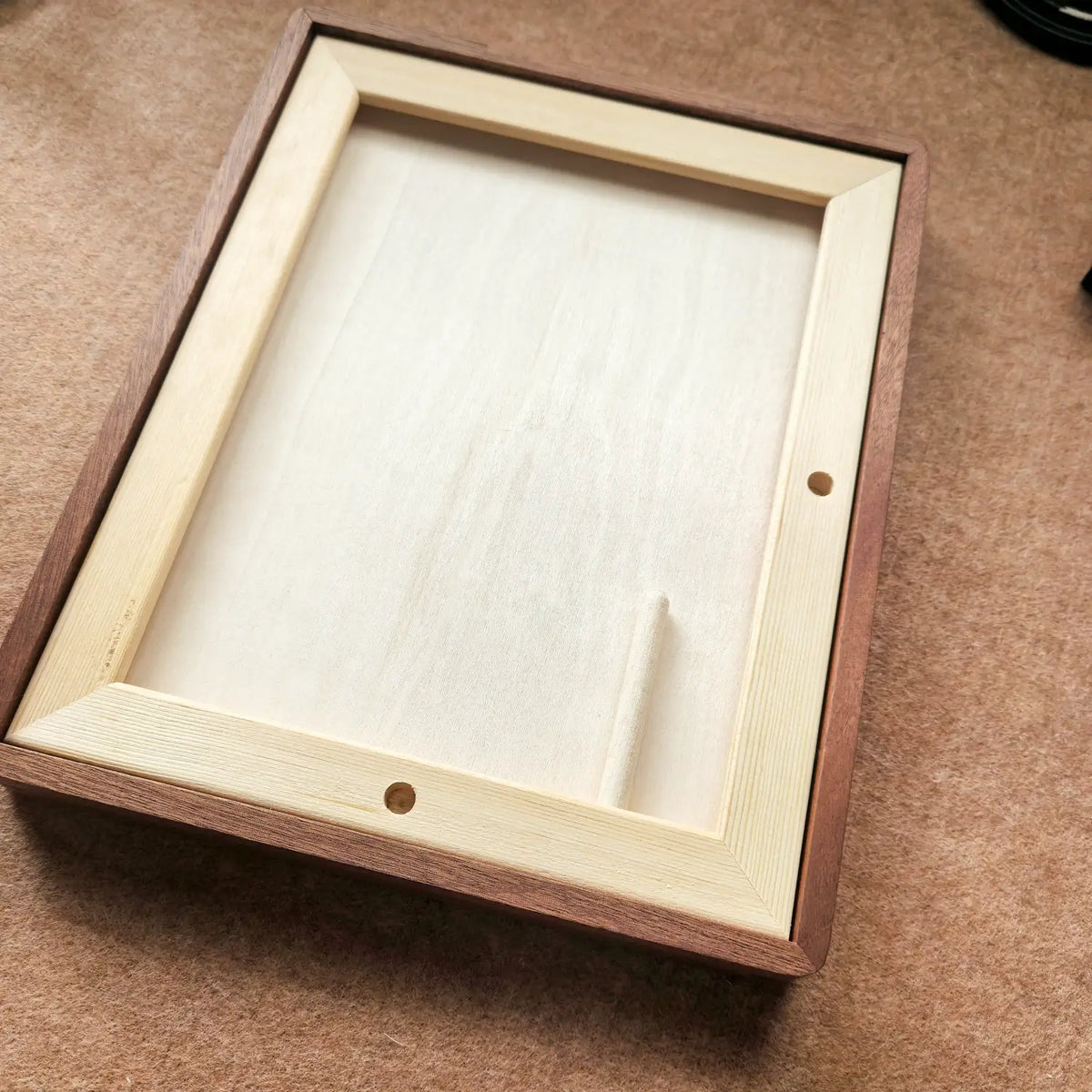 Wall-mounted “岁岁长安” Chinese calligraphy artwork in a solid ebony wood frame. A rectangular wooden picture frame with a dark brown outer border and a light natural wood inner frame, shown on a brown textured surface.